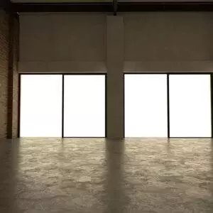 The empty room features large windows that flood the space with light, highlighting the polished concrete floor enhanced by a premium concrete coating. An exposed brick wall stands prominently on the left, bringing a touch of Oregon's industrial charm to life.